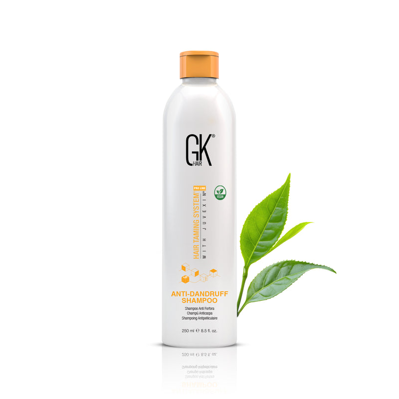 GK Hair Anti-Dandruff Shampoo 250 ml white bottle with an orange cap and vegan badge, green tea leaves beside it