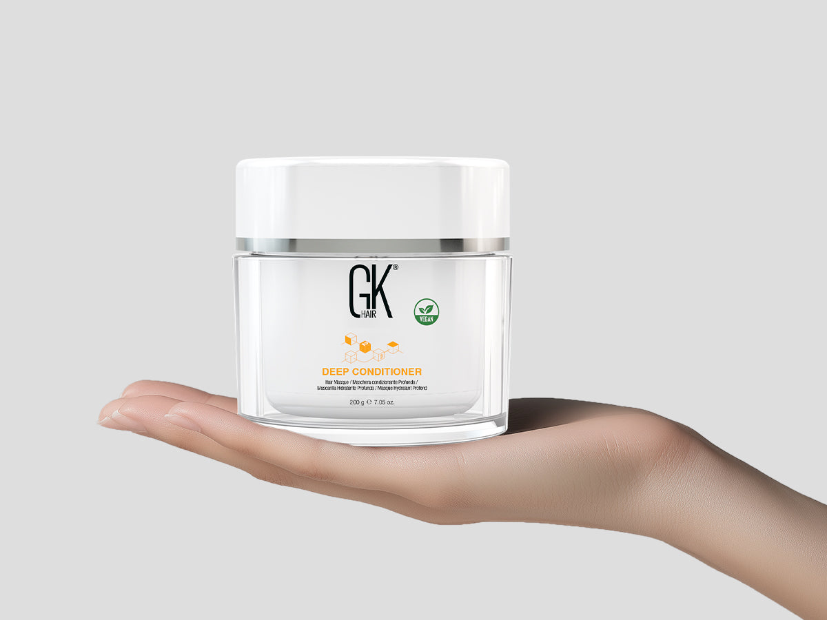 A hand holding a jar of GK Hair Deep Conditioner, featuring a clean design with a white lid and vegan certification label.