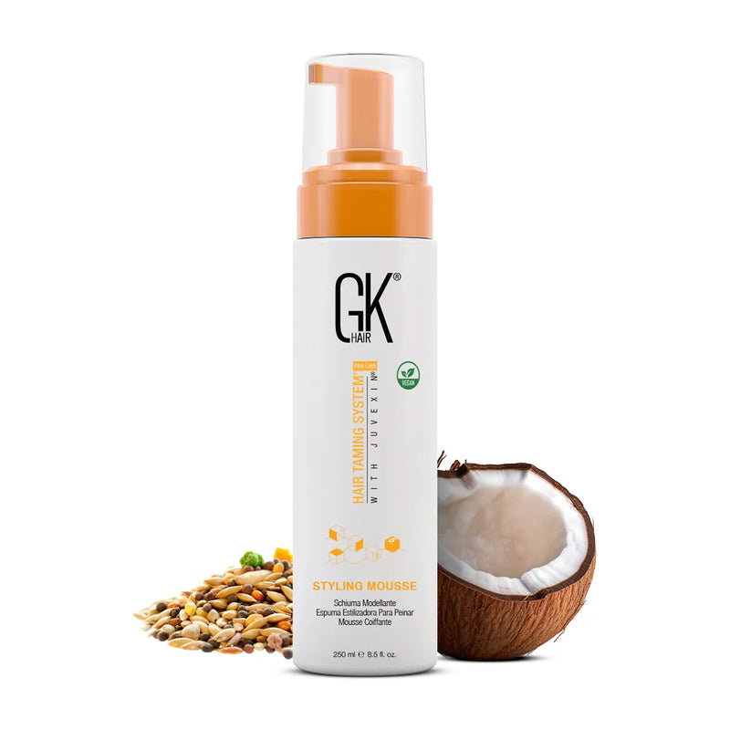 GK Hair Styling Mousse 250 ml white bottle with orange pump and vegan badge, beside a halved coconut and mixed seeds